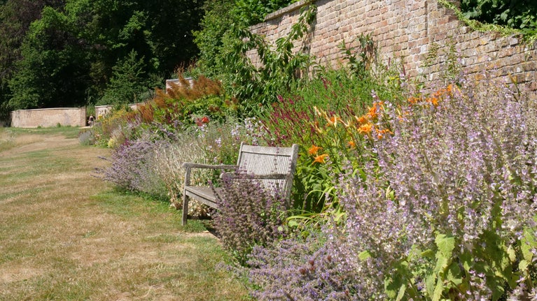A flower border in late summer with a bench and brick garden wall at Newark Park